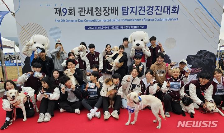 제9회 관세청장배 탐지견경진대회배너 앞에서 학생들과 반려견들이 단체 사진을 찍고 있다.
